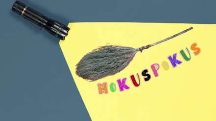 Im Lichtkegel einer Taschenlampe ist ein Hexenbesen und der Schriftzug "Hokuspokus" zu sehen.