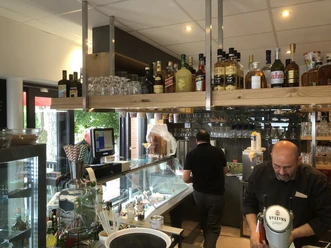 Theke im Eiscafé mit Spirituosenregal, Gläsern, Eistheke und Personal hinter dem Tresen.