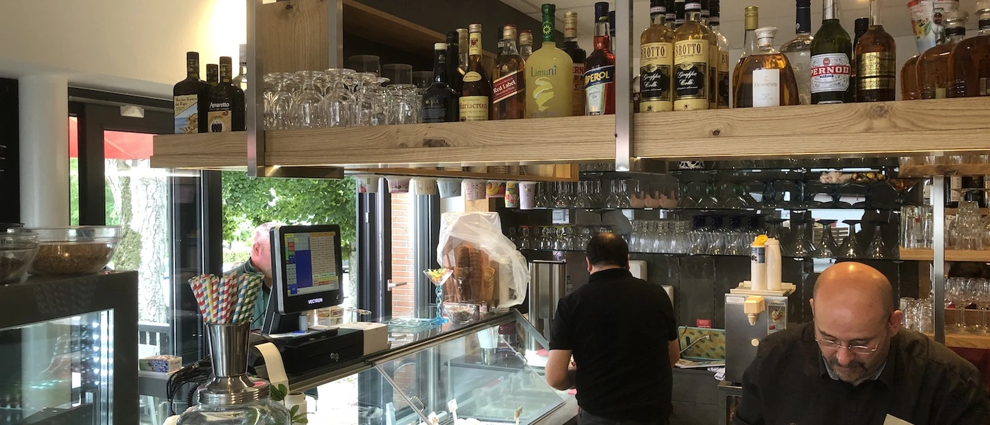 Theke im Eiscafé mit Spirituosenregal, Gläsern, Eistheke und Personal hinter dem Tresen.