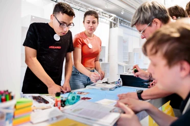 Jugendliche basteln gemeinsam an einem Tisch im hellen Museumsworkshop