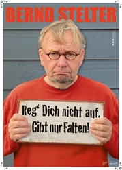 Bernd Stelter mit ernster Miene hält ein Schild: Reg’ Dich nicht auf. Gibt nur Falten!