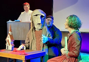 Theaterszene aus „Der Elefantenmensch“ mit maskierter Figur und Ensemble auf der Bühne