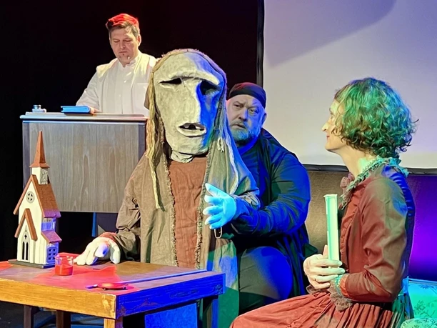Theaterszene aus „Der Elefantenmensch“ mit maskierter Figur und Ensemble auf der Bühne