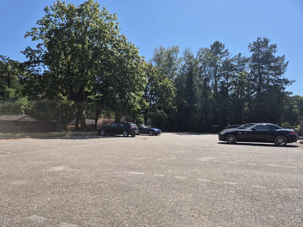 Öffentlicher Parkplatz in Rastede mit blauem Parkschild, Bäumen, Autos und Wohngebäuden.