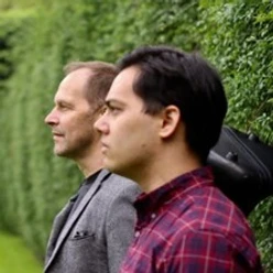 Zwei Musiker im Profil vor grüner Hecke, mit kariertem Hemd und grauem Sakko