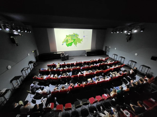 Publikum in roten Kinosesseln verfolgt eine Präsentation in moderner Eventlocation