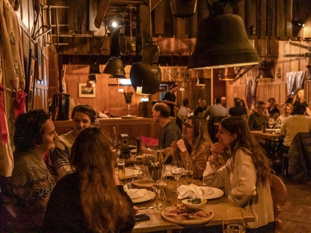 Gäste beim Essen in der warm beleuchteten Titlis-Hütte mit Holzinterieur und Kuhglocken