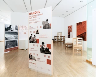 Poster über Hangul-Generationsreihe und Holzstühle im Museum.