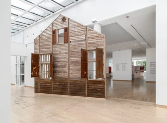 Alte Holzwandinstallation in hellem Galerieraum.