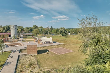 Ansicht des Archäologieparks mit Holzkubus, Zelten und Grabungsstelle