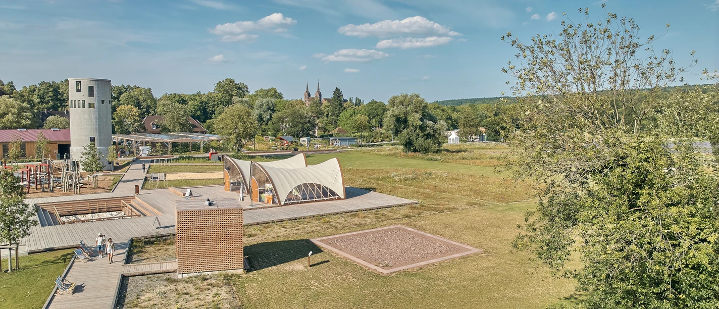 Ansicht des Archäologieparks mit Holzkubus, Zelten und Grabungsstelle