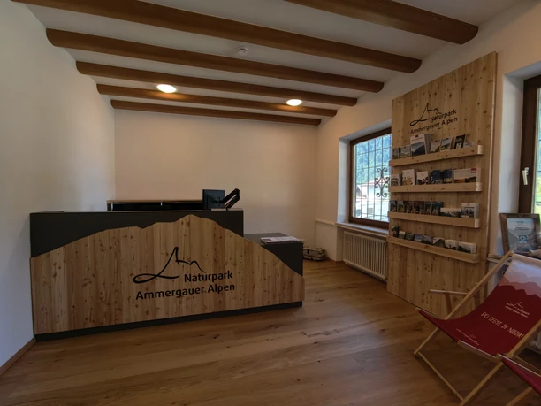 Moderner Holz-Empfangstresen mit Naturpark Ammergauer Alpen Logo und Prospektwand in der Tourist-Information Ettal