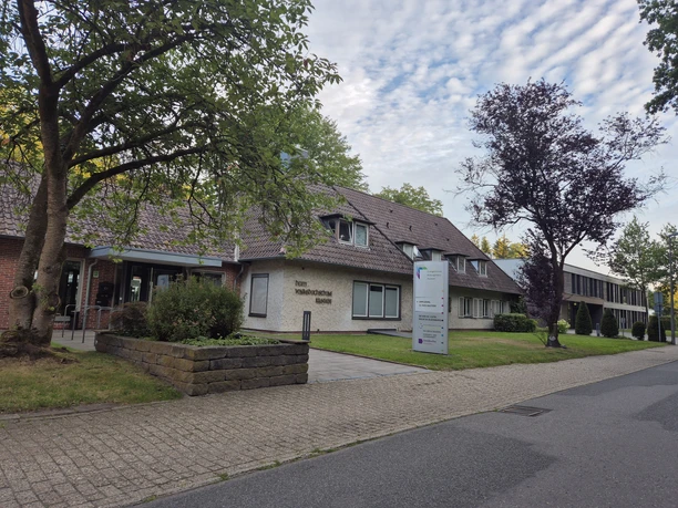 Evangelisches Bildungshaus Rastede mit Eingang, Schild und Bäumen vor bewölktem Himmel.