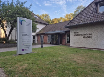 Eingang des Evangelischen Bildungshauses Rastede mit Wegweiser und Backsteingebäude.