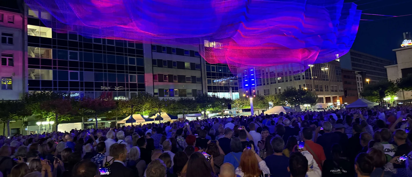 Leuchtende Netzinstallation über einer Menschenmenge bei Nacht in Frankfurt