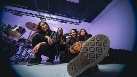 Vier Musikerinnen im Proberaum mit Schlagzeug und Gitarre.