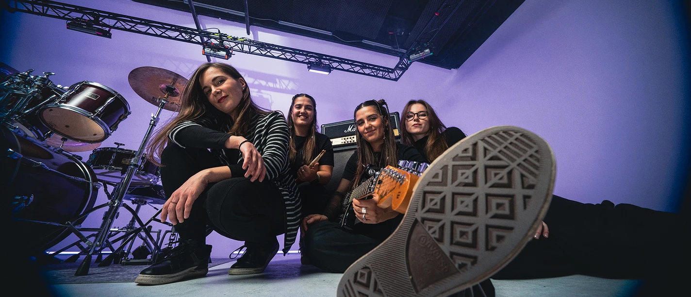 Vier Musikerinnen im Proberaum mit Schlagzeug und Gitarre.