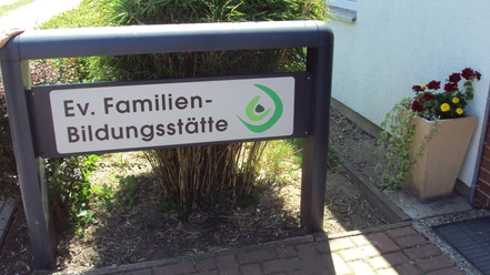 Schild der Ev. Familien-Bildungsstätte Salzgitter vor dem Eingang mit Blumenkübel.