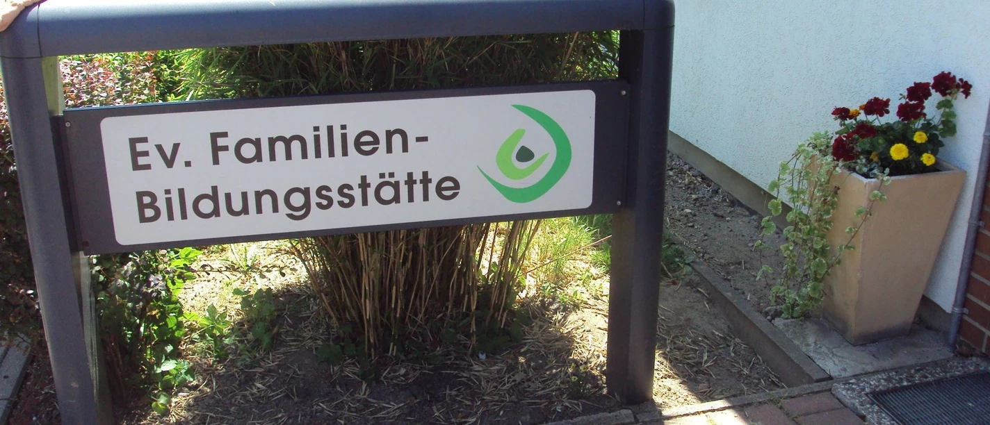 Schild der Ev. Familien-Bildungsstätte Salzgitter vor dem Eingang mit Blumenkübel.