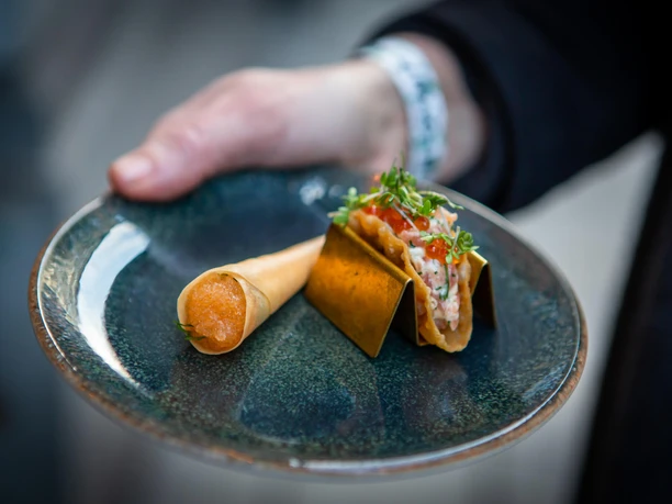 Hand reicht dunklen Teller mit zwei fein angerichteten Gourmet-Häppchen beim Moveat in Köln