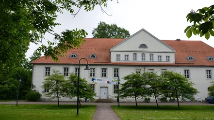 Kniestedter Herrenhaus mit rotem Dach, weißen Fassaden und Bäumen im Vordergrund.