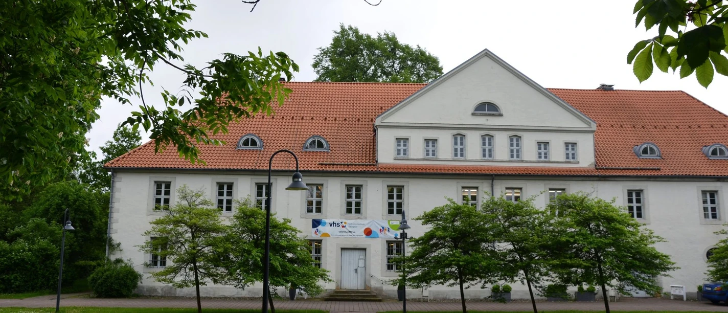 Kniestedter Herrenhaus mit rotem Dach, weißen Fassaden und Bäumen im Vordergrund.