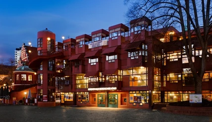 Abendansicht des Bürgerhauses Bergischer Löwe mit beleuchteter roter Fassade