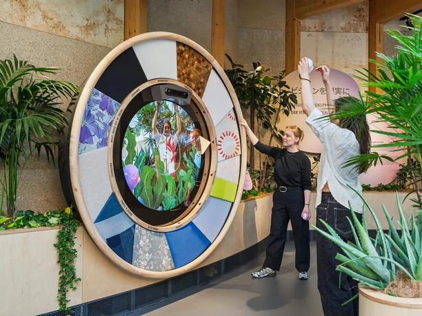 Visitors at an interactive fashion installation featuring fabric swatches and plants