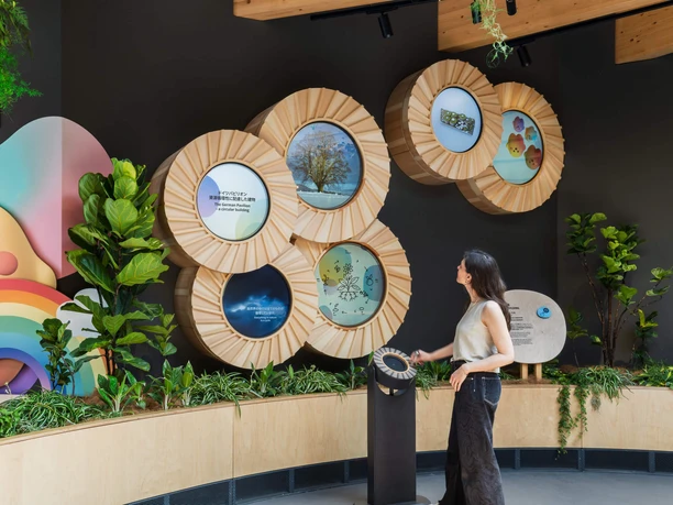 Besucherin vor interaktiver Ausstellung mit runden Holzmodulen und Pflanzen