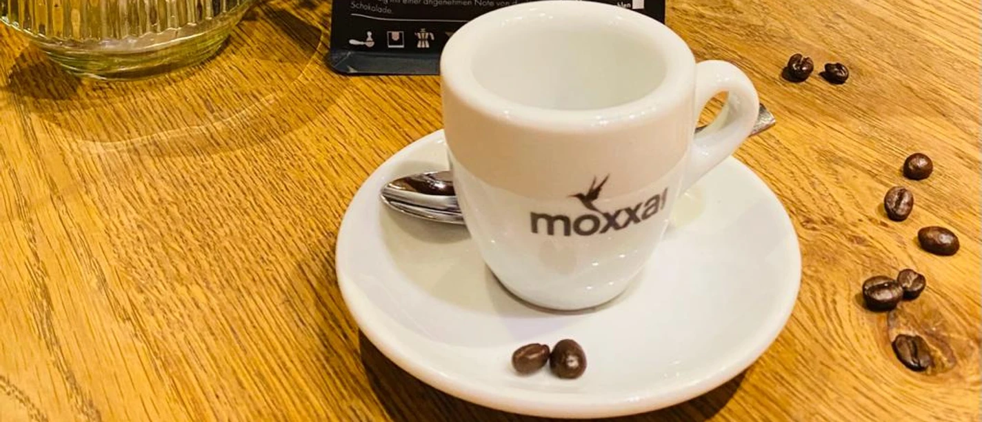 Espressotasse vor Café-de-la-Gomera-Packungen, Bohnen und Blumen auf Holztisch