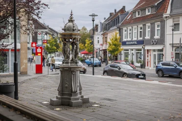 Wallace-Brunnen aus Gusseisen an einer belebten Straße in Burscheid.