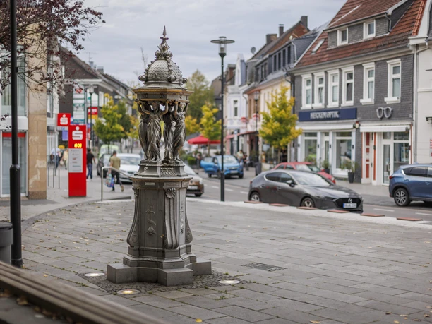 Wallace-Brunnen aus Gusseisen an einer belebten Straße in Burscheid.
