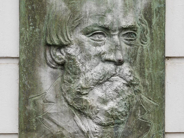 Bronzerelief mit Porträt von Montanus an einer hellen Hauswand in Burscheid