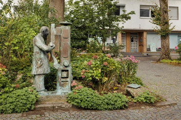 Bronzefigur eines Schusters an einer Maschine zwischen Pflanzen in Wermelskirchen