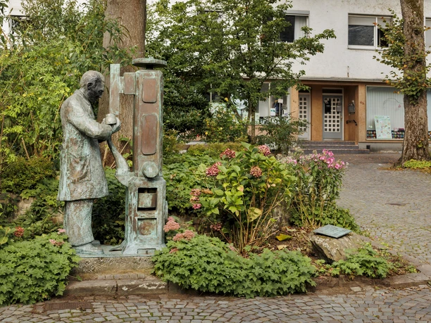 Bronzefigur eines Schusters an einer Maschine zwischen Pflanzen in Wermelskirchen