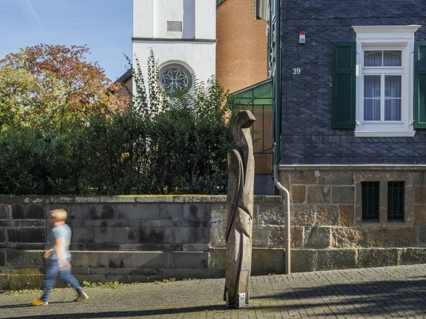 Skulptur „Metamorphose“ an einer Hausfassade in Wermelskirchen, Passant im Vordergrund