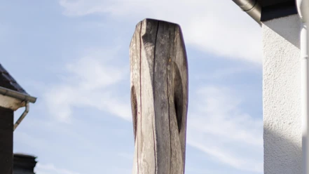 Hohe Holzskulptur vor Hecke und Hausfassade unter hellem Himmel in Wermelskirchen