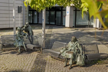 Bronzeskulptur „Begegnung“ mit drei Figuren auf Bänken vor einem Gebäude in Wermelskirchen
