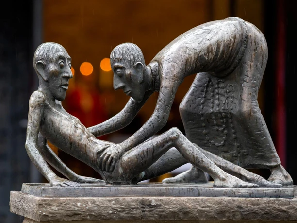 Bronzeskulptur von Toni Zenz mit helfender Figur vor der Wallfahrtskirche Marienheide