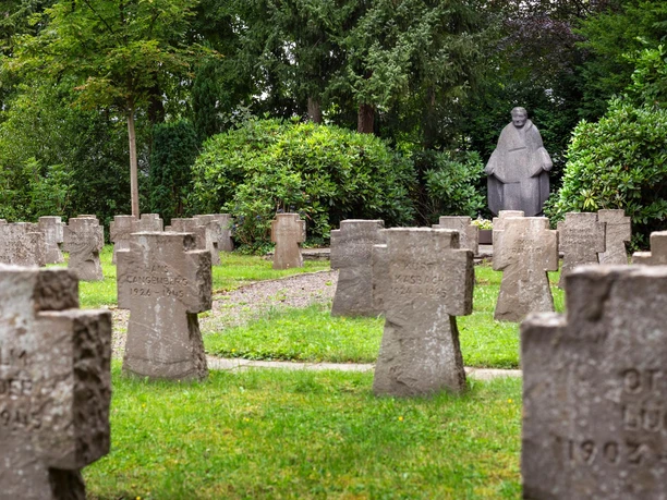 Steinkreuze auf grünem Friedhof, dahinter die Skulptur Mutter Erde von Jupp Rübsam