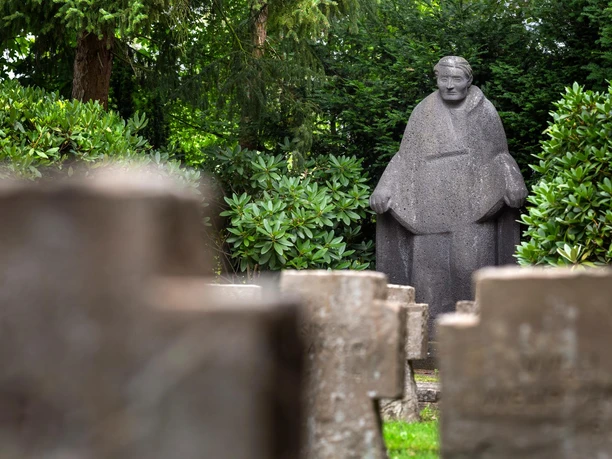 Steinskulptur „Mutter Erde“ von Jupp Rübsam zwischen Grün und Grabsteinen