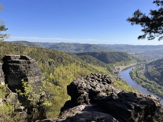 Aussicht auf einen Fluss, umgeben von bewaldeten Bergen und Felsen unter klarem blauen Himmel.