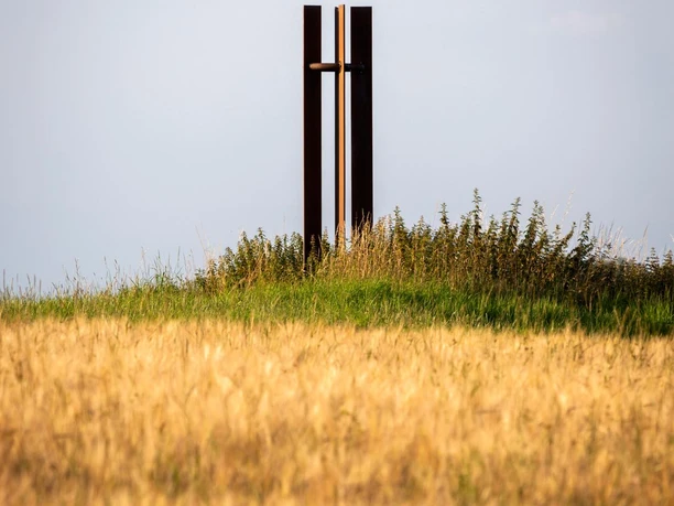 Friedens-Stele aus dunklem Metall auf einer Wiese vor hellem Himmel