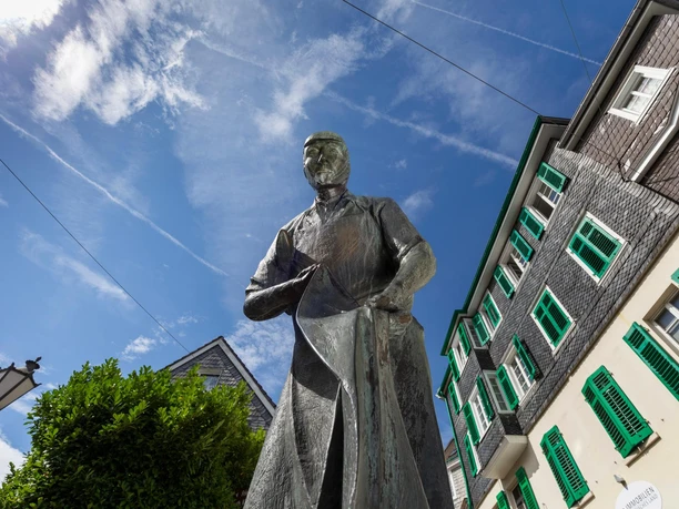 Bronzestatue Der Weber vor Schieferhäusern in Hückeswagen unter blauem Himmel