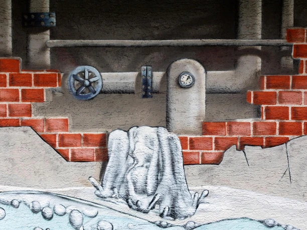 Graffiti mit Ziegelmauer, Rohren und sprudelndem Wasser am Regenüberlaufbecken