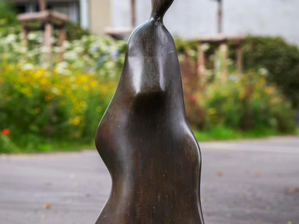 Bronzeskulptur „Auf dem Weg“ von Bernhard Guski vor Grünanlage und Straße in Hückeswagen
