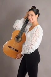 Emma Campàs lächelt mit klassischer Gitarre vor grauem Hintergrund