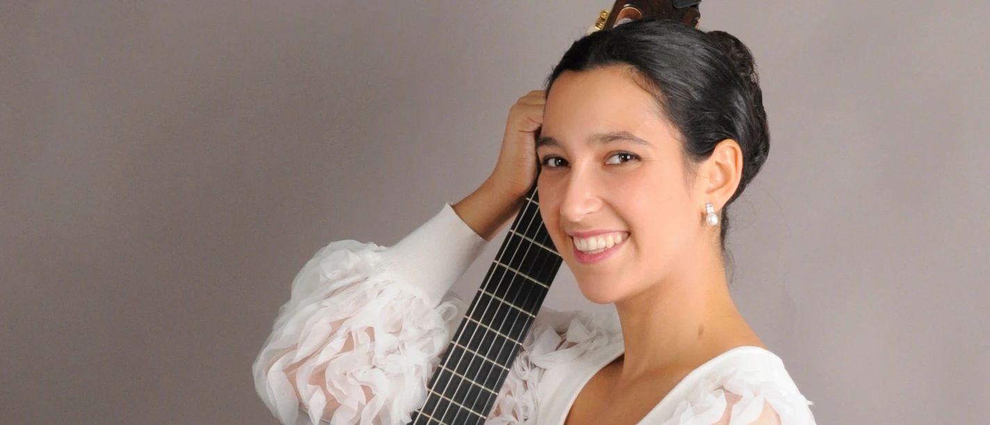 Emma Campàs lächelt mit klassischer Gitarre vor grauem Hintergrund