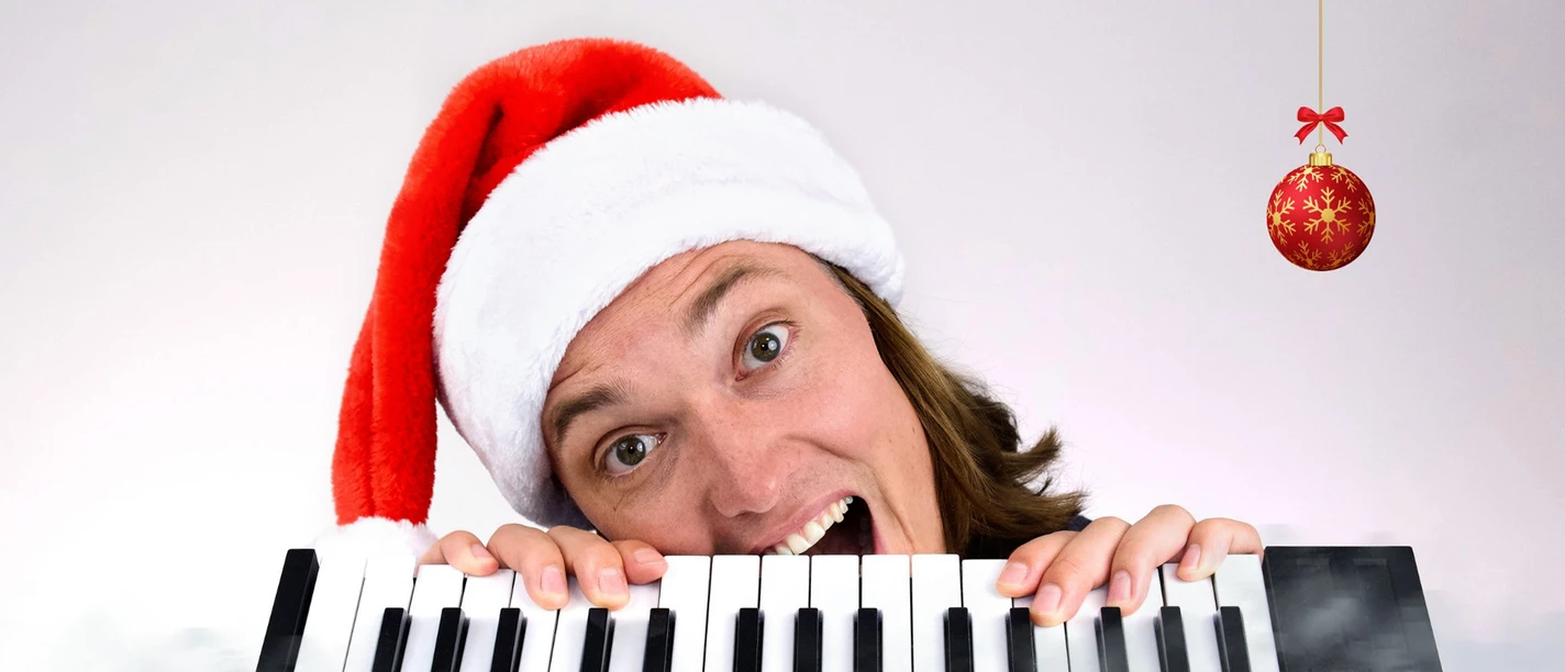 Eine Person mit Weihnachtsmannmütze hält ein Keyboard; daneben hängt eine rote Christbaumkugel.