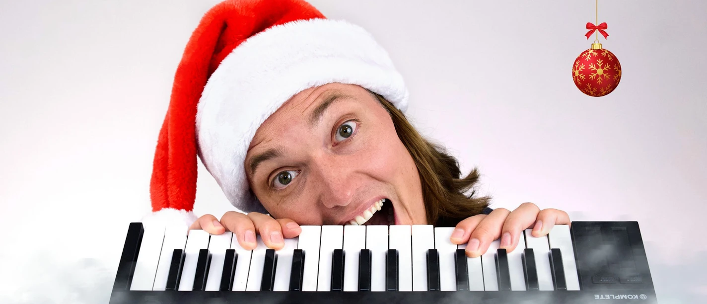 al-x-mas-03_c_rachele-pedrocchi Eine Person mit Weihnachtsmannmütze hält ein Keyboard; daneben hängt eine rote Christbaumkugel.